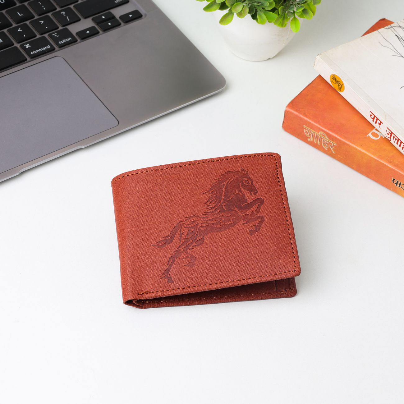Stylish leather wallet with horse engraving on a modern desk with laptop and books.
