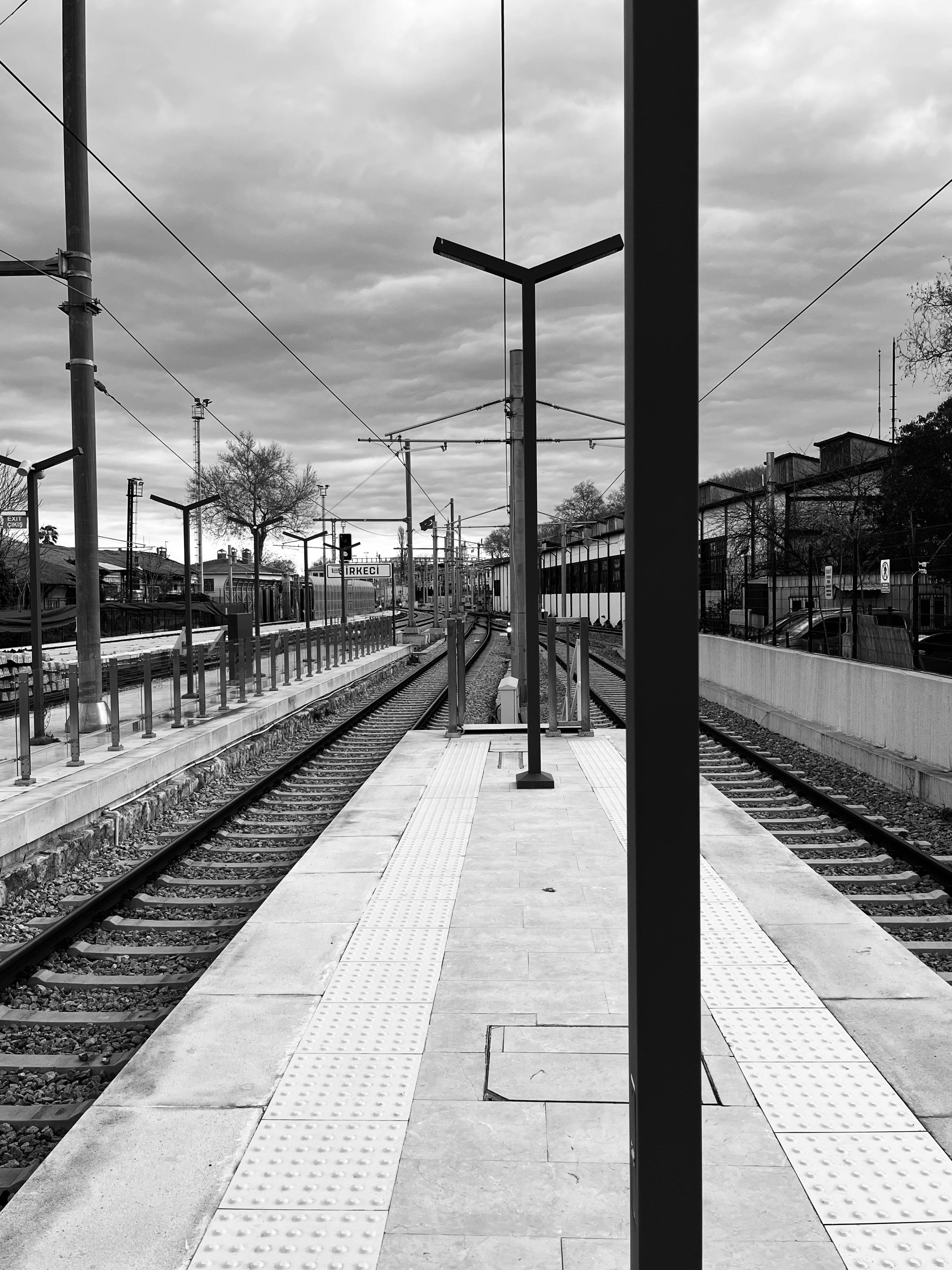 Gratis Gambar monokrom jalur kereta api dan peron yang sepi di bawah langit berawan. Foto Stok