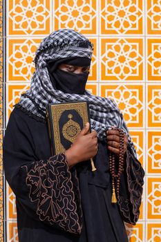 A woman in traditional clothing holds a holy book and prayer beads.