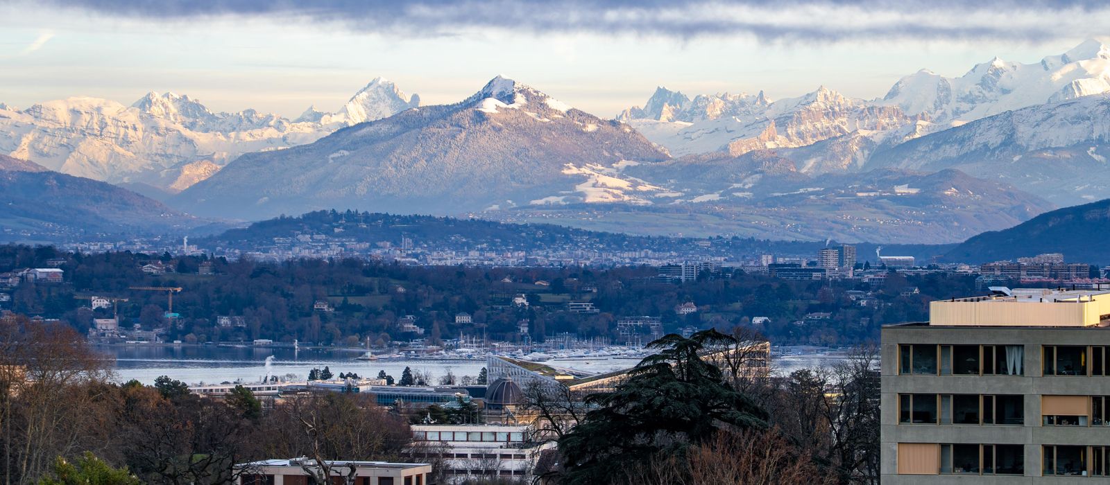 A breathtaking view of Geneva with Swiss Alps backdrop under a cloudy sky at day. — flights from London to Geneva