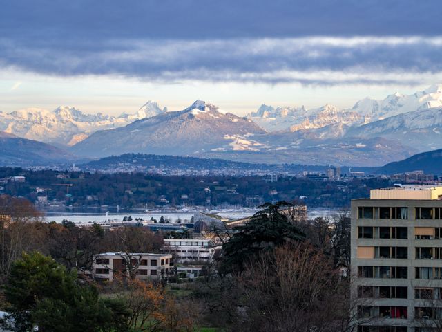 A breathtaking view of Geneva with Swiss Alps backdrop under a cloudy sky at day.