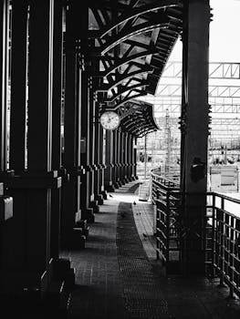 A black and white view of a train station platform with a clock and architectural elements.