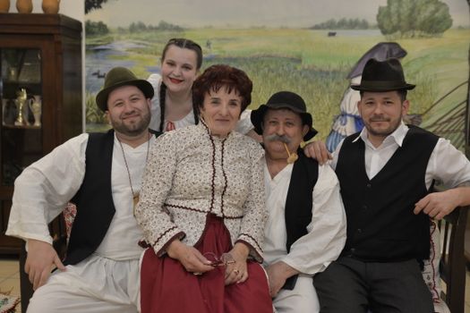 A Hungarian family dressed in traditional folk clothing poses indoors, exuding cultural heritage.