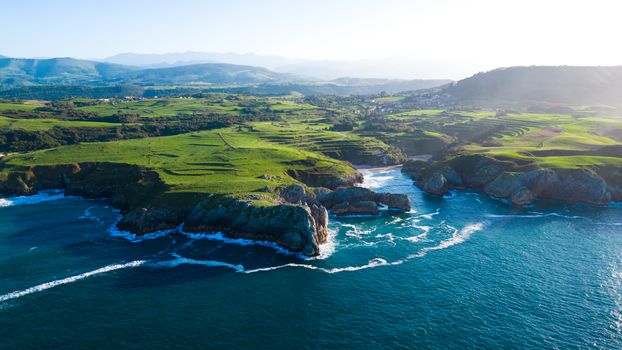 Stunning aerial shot of the rugged coastline in Asturias, Spain with verdant cliffs and blue waters.