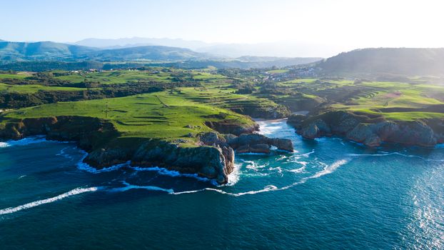 A stunning aerial view of the lush green coastline of Asturias, Spain, with waves crashing against cliffs.