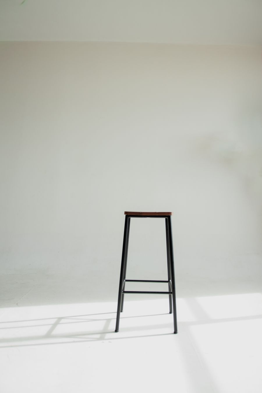 Slim black stool against a white wall — photo by Bruno Casttro on Pexels