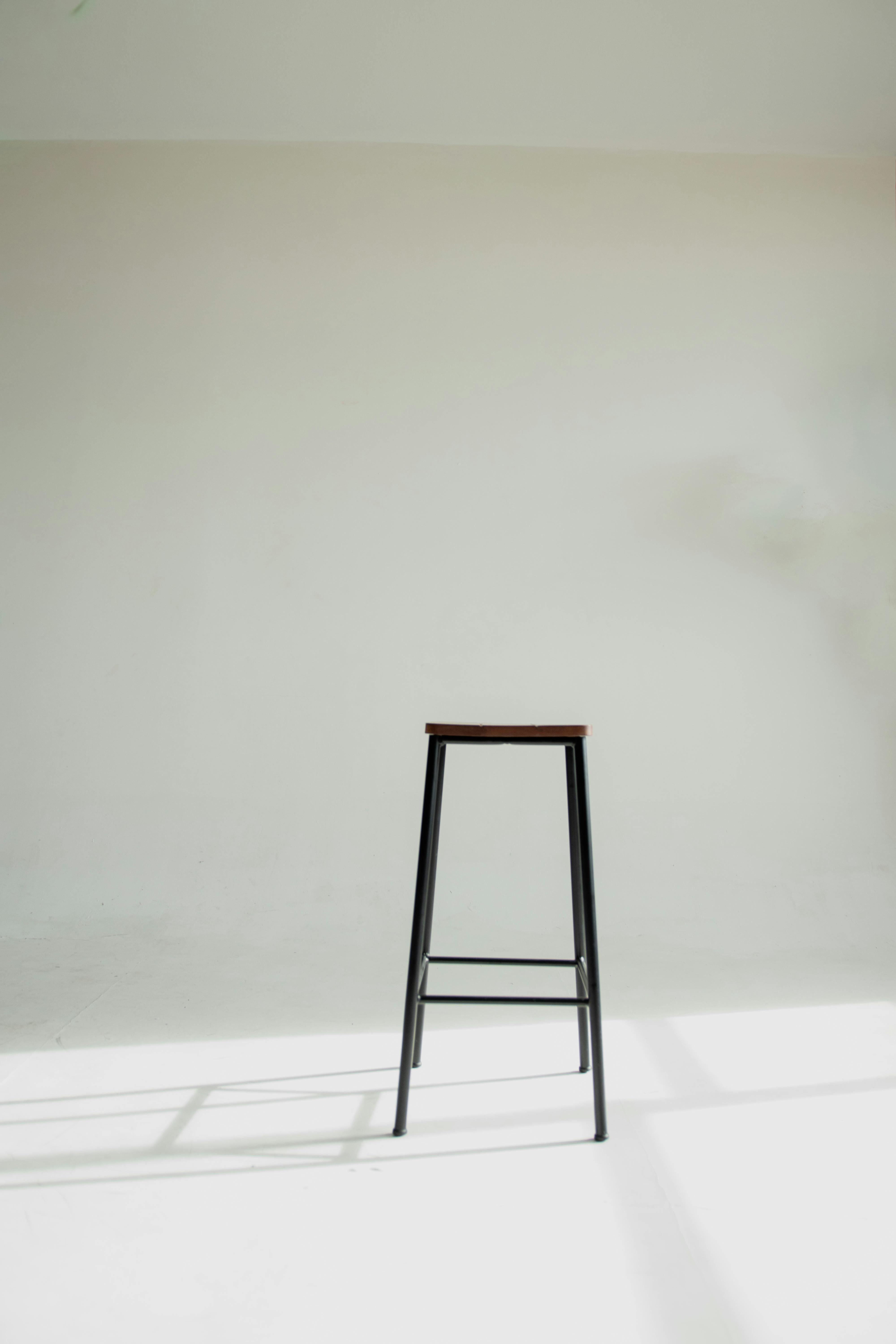 Free A simple black stool against a white wall, highlighting modern minimalist design. Stock Photo