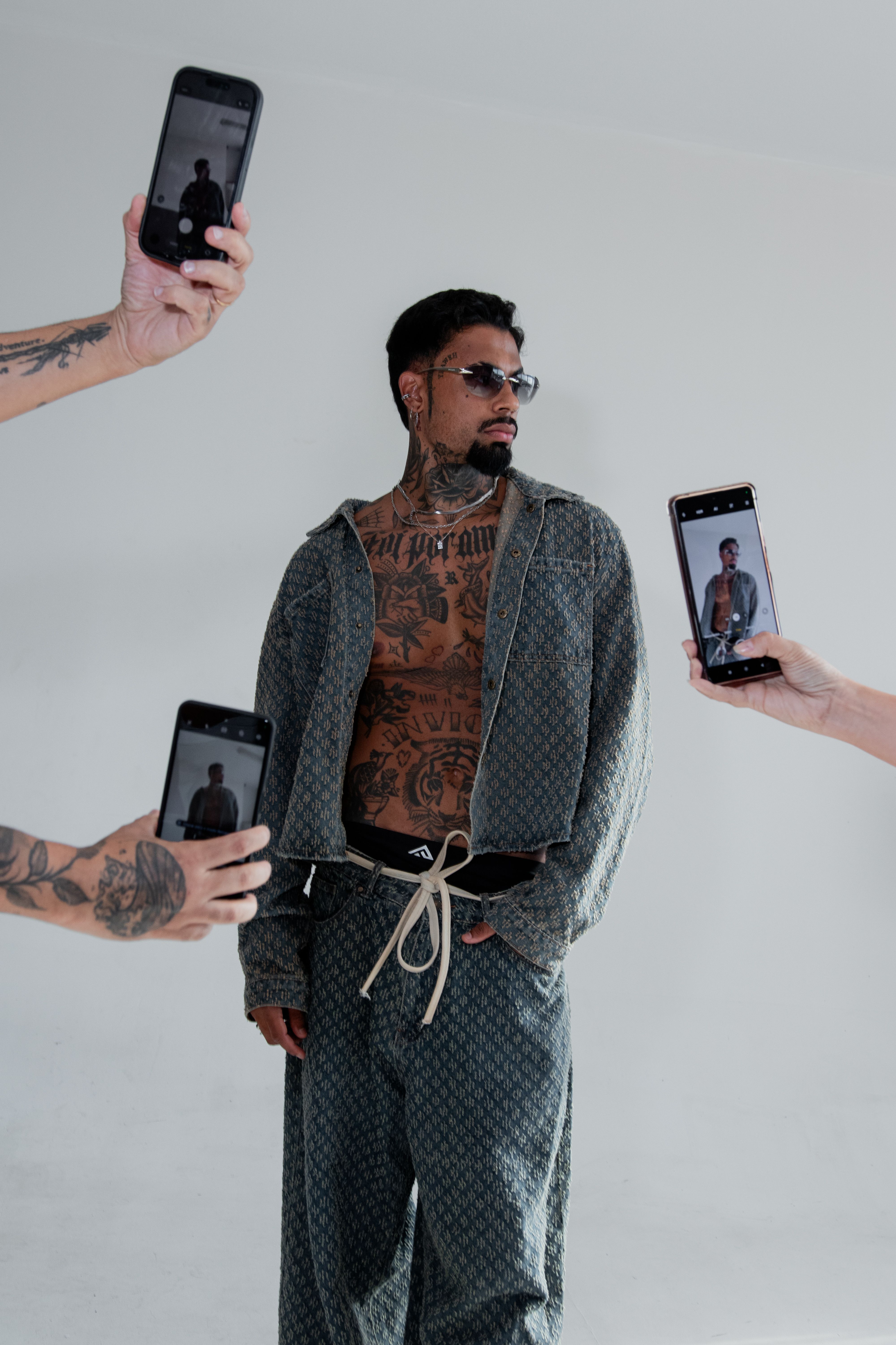 Trendy tattooed man posing with phones capturing his style indoors.