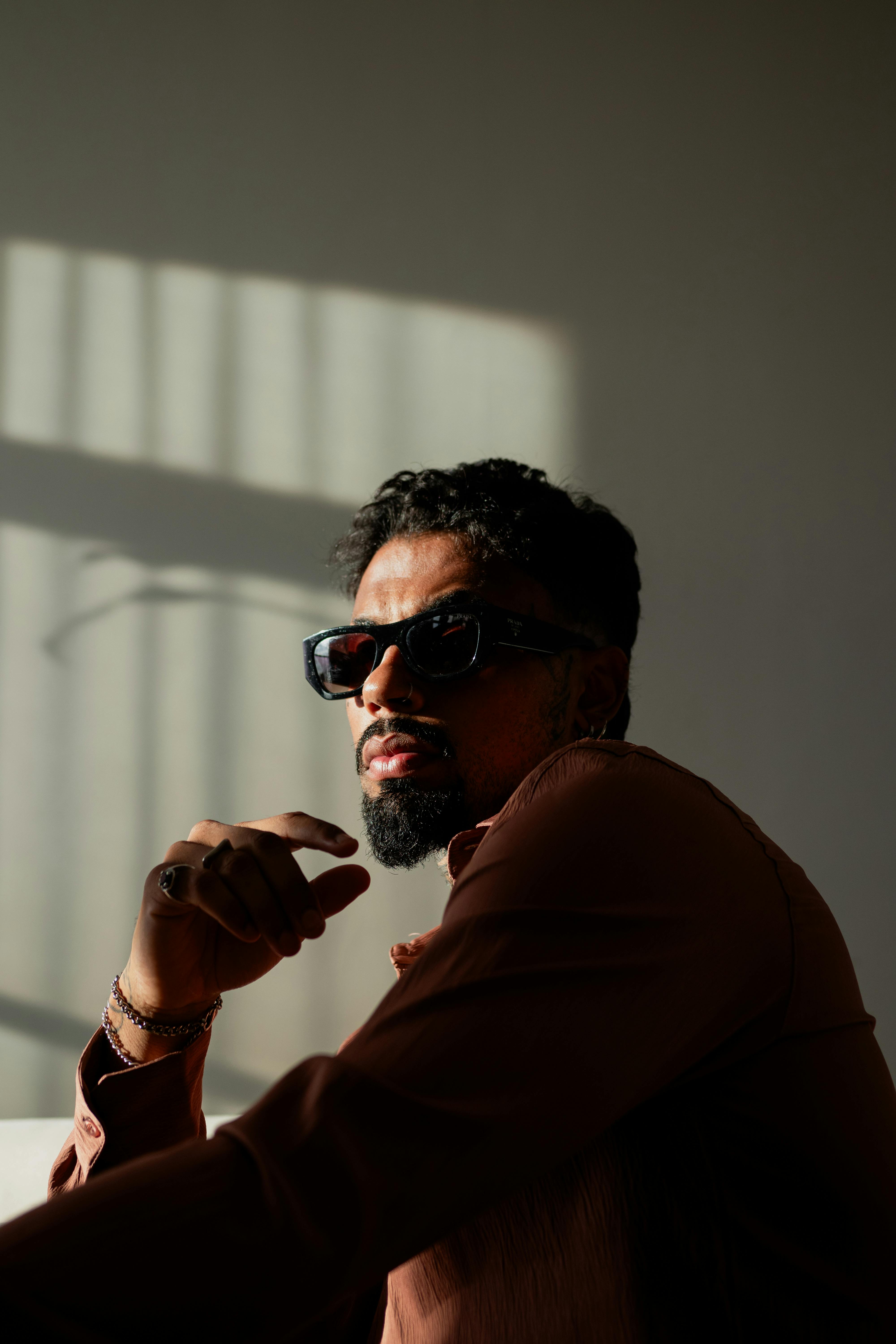 Free Portrait of a fashionable adult man in sunglasses and shadowy lighting, expressing confidence. Stock Photo