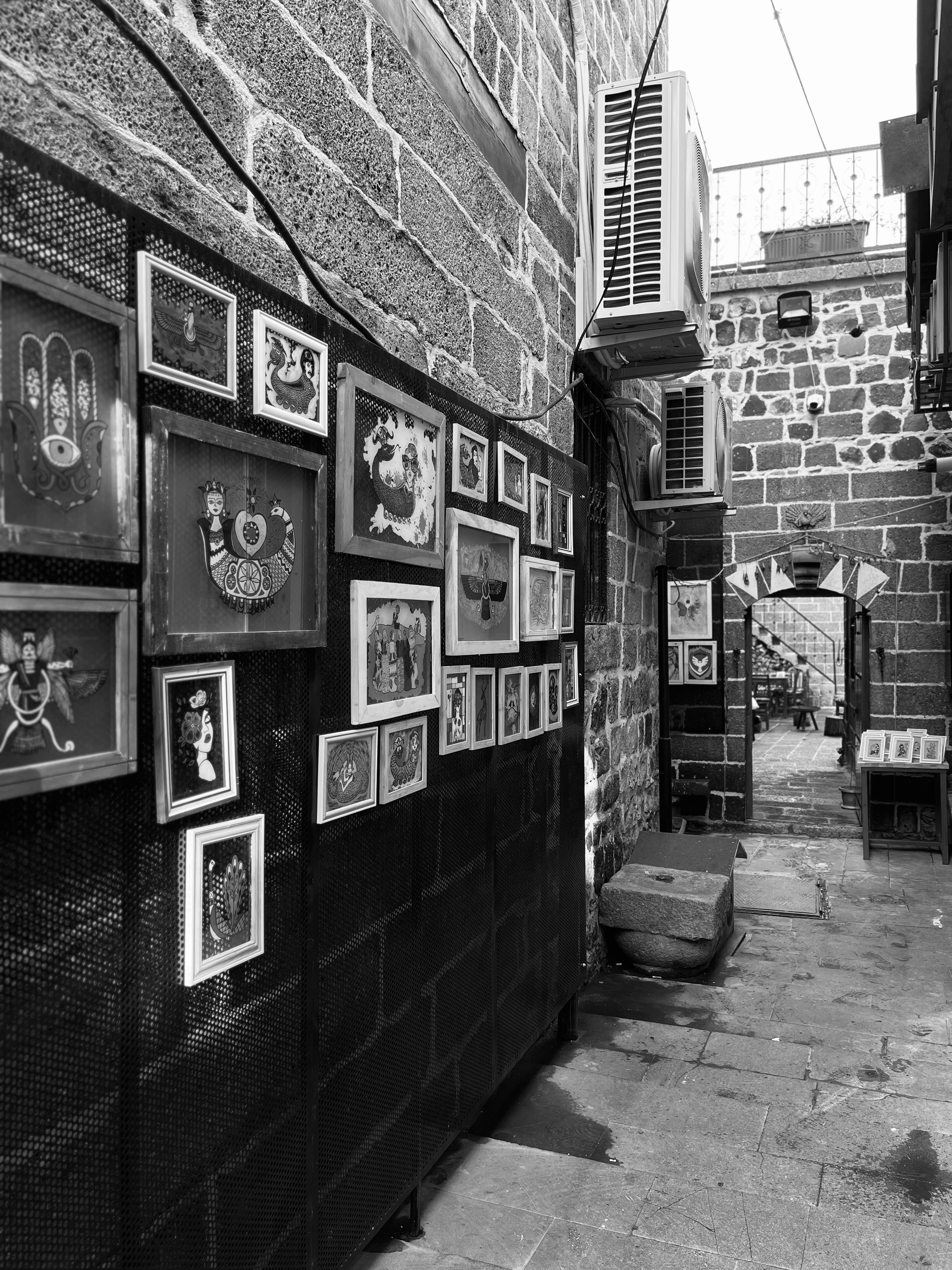 Monochrome alley with framed artwork on stone walls, showcasing urban creativity.