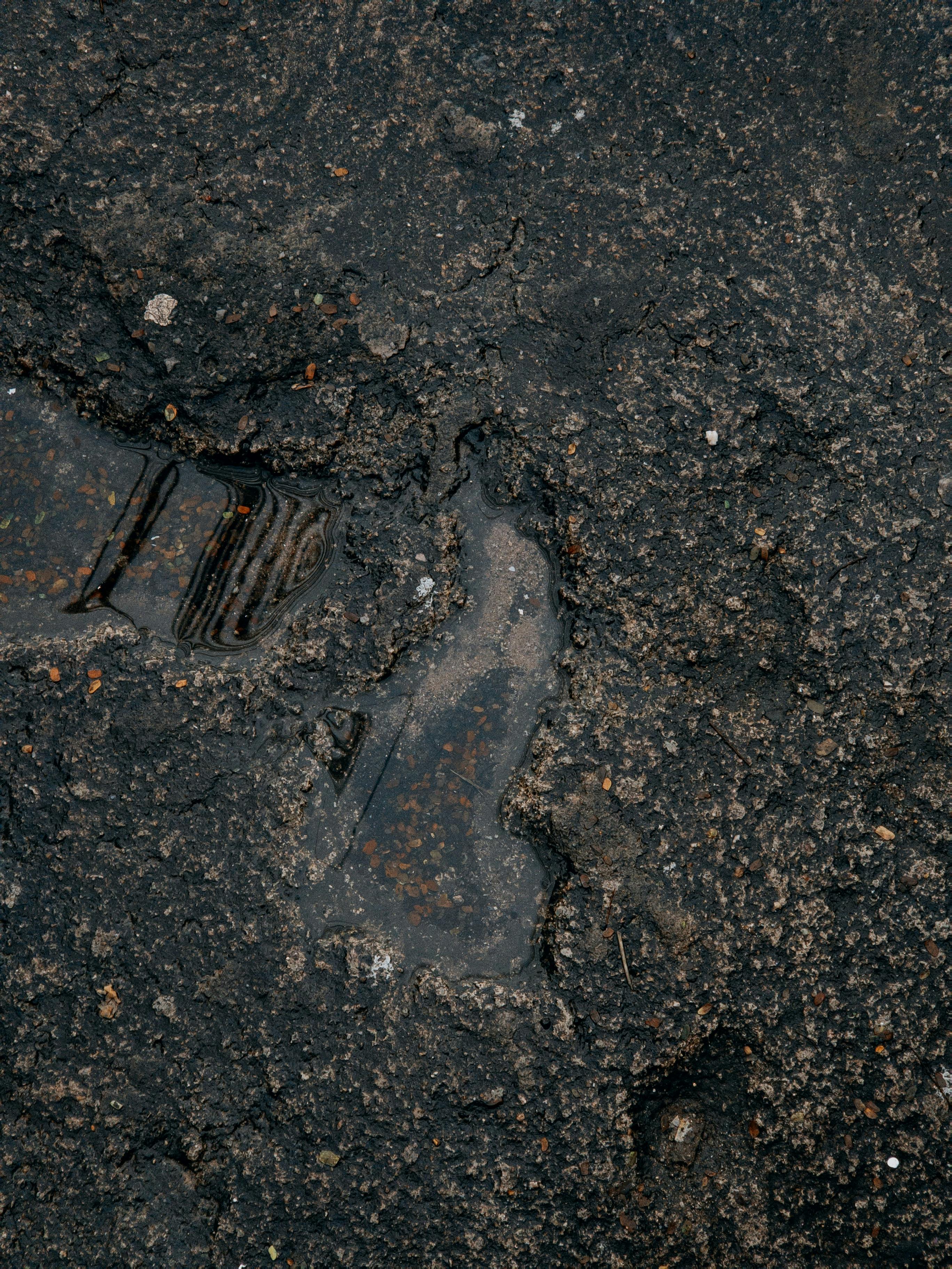 Ücretsiz Koyu dokulu asfaltın yakın çekim görüntüsü; üzerinde küçük bir su birikintisi ve lastik izleri görünüyor. Stok Fotoğraflar