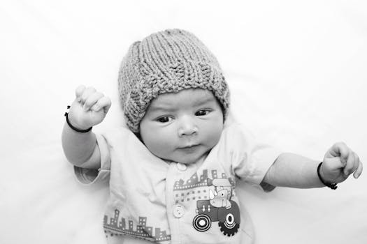 Adorable baby wearing a knitted hat, lying on a white surface, with a playful expression.