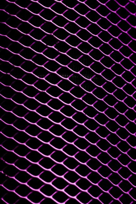 Fotomural Vista de primer plano de un patrón de rejilla metálica iluminada en color púrpura con un fondo oscuro.
