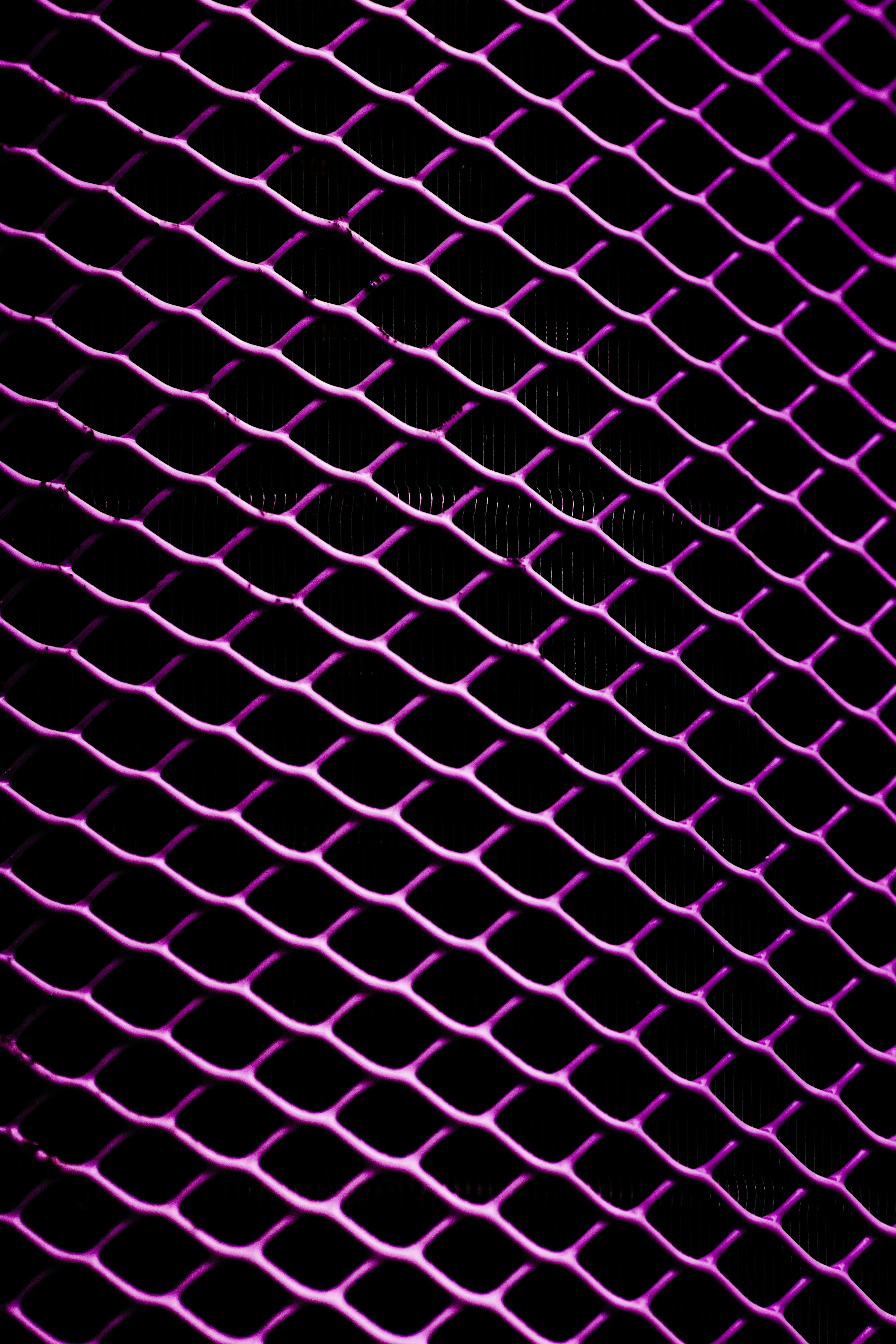 Gratis Vista ravvicinata di un motivo a griglia metallica illuminato di viola con sfondo scuro. Foto a disposizione