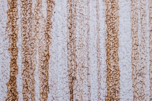 Close-up of a textured wall with brown vertical rust-like stains creating an abstract pattern.