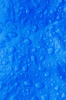 Close-up view of water droplets on a vibrant blue textured surface, creating a refreshing abstract background.