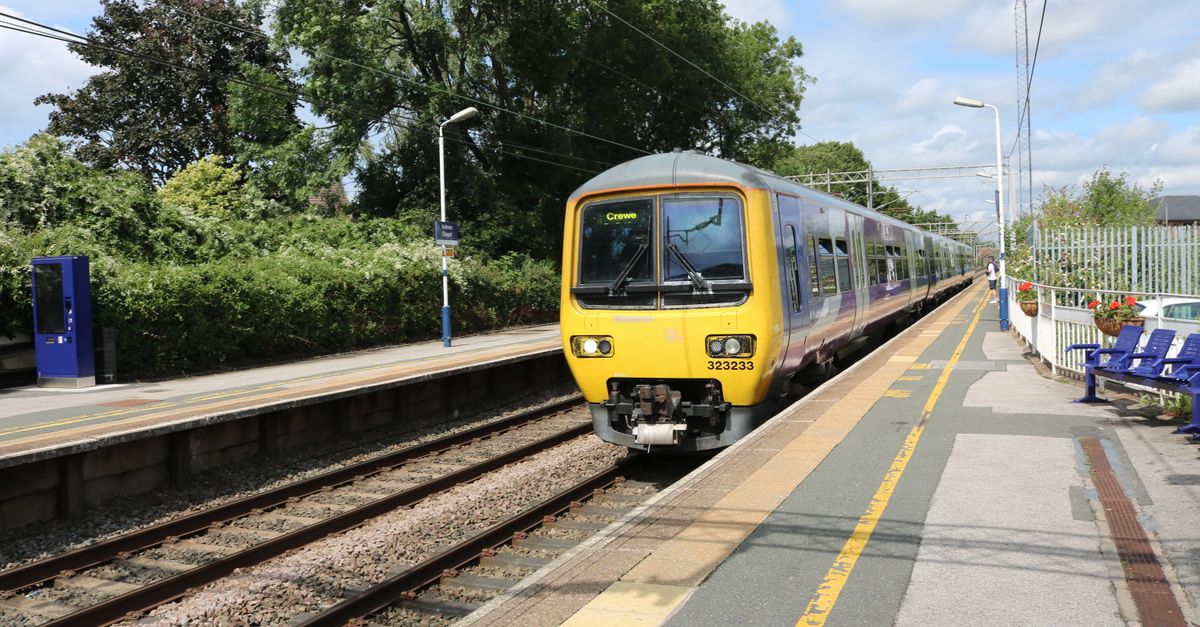A commuter train arrives at Holmes Chapel station under a sunny sky in England.