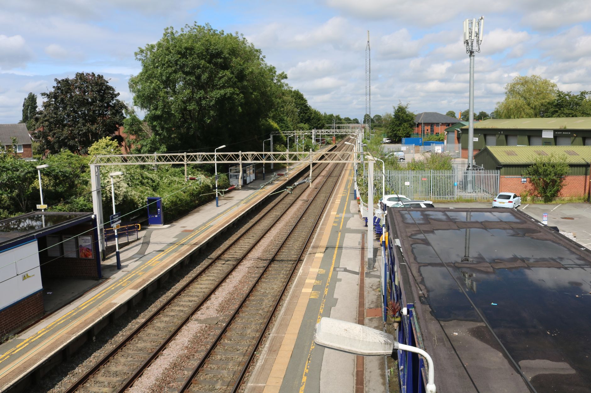 Aerial view of Holmes Chapel train station with tracks and platforms on a sunny day.