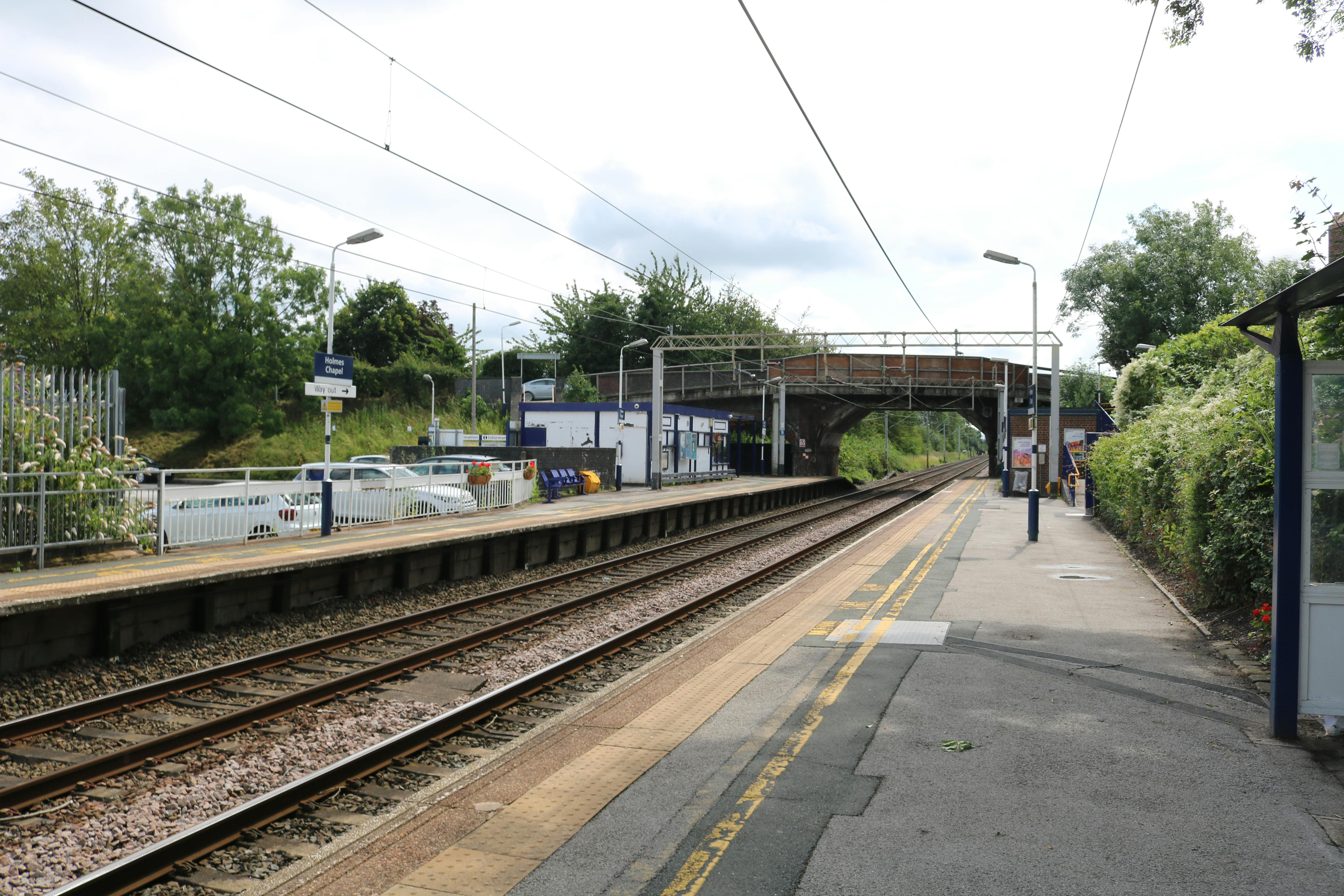 Holmes Chapel train station in England, showing an empty platform and tracks on a sunny day.