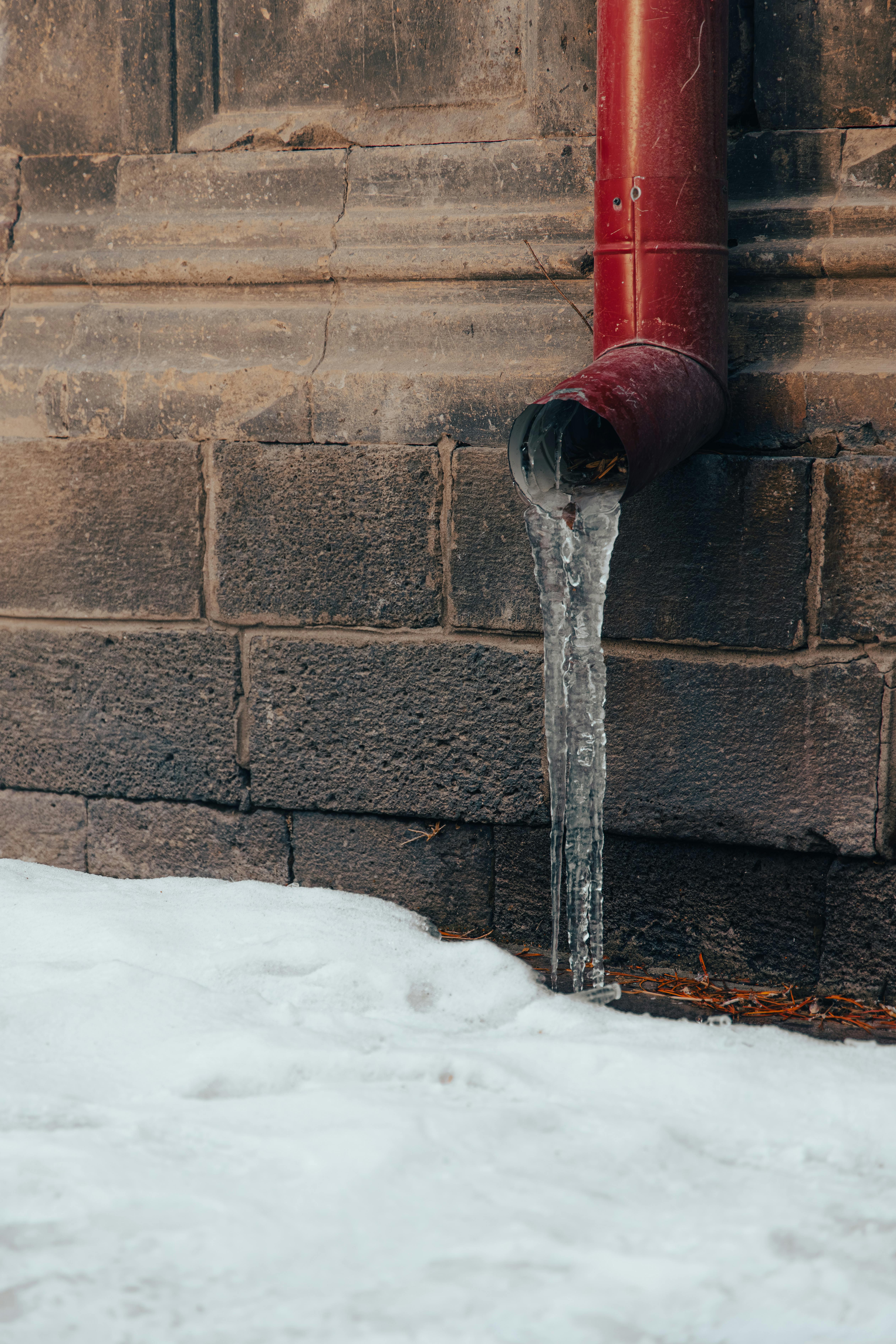 Free Icy water pipe with dripping icicles against a stone wall in Kars, Türkiye during winter. Stock Photo
