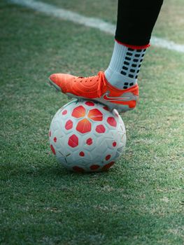 A soccer player's foot in bright orange cleats on a soccer ball on grass.