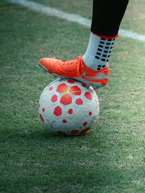 Free A soccer player's foot in bright orange cleats on a soccer ball on grass. Stock Photo