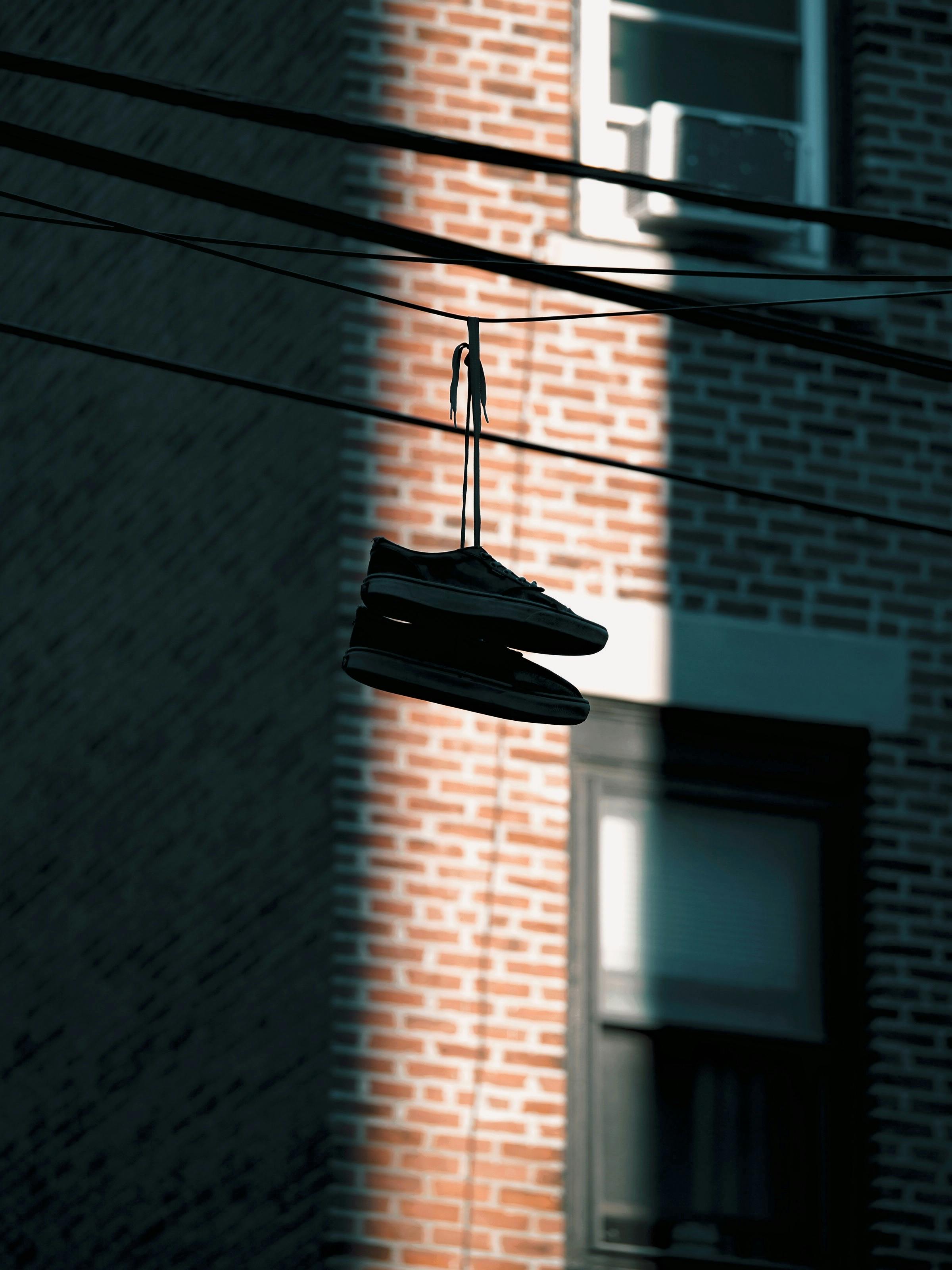 Gratis Et par joggesko som henger på en wire med en mursteinsbygning som bakgrunn i Boston. Arkivbilde