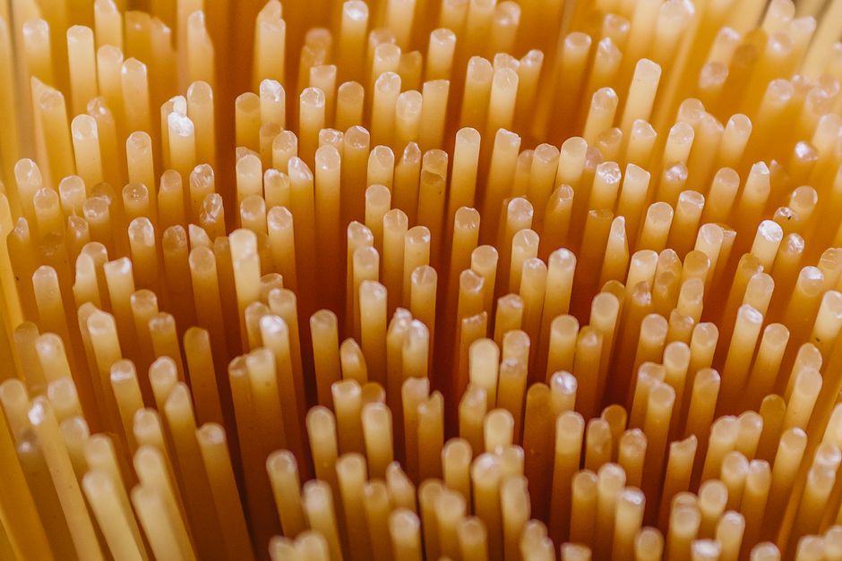 Bundles of dried spaghetti strands next to a cooked, sauced portion twirled on a fork.
