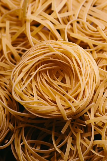 Coiled nests of dry capellini pasta next to a plated serving tossed with olive oil, garlic, and parsley