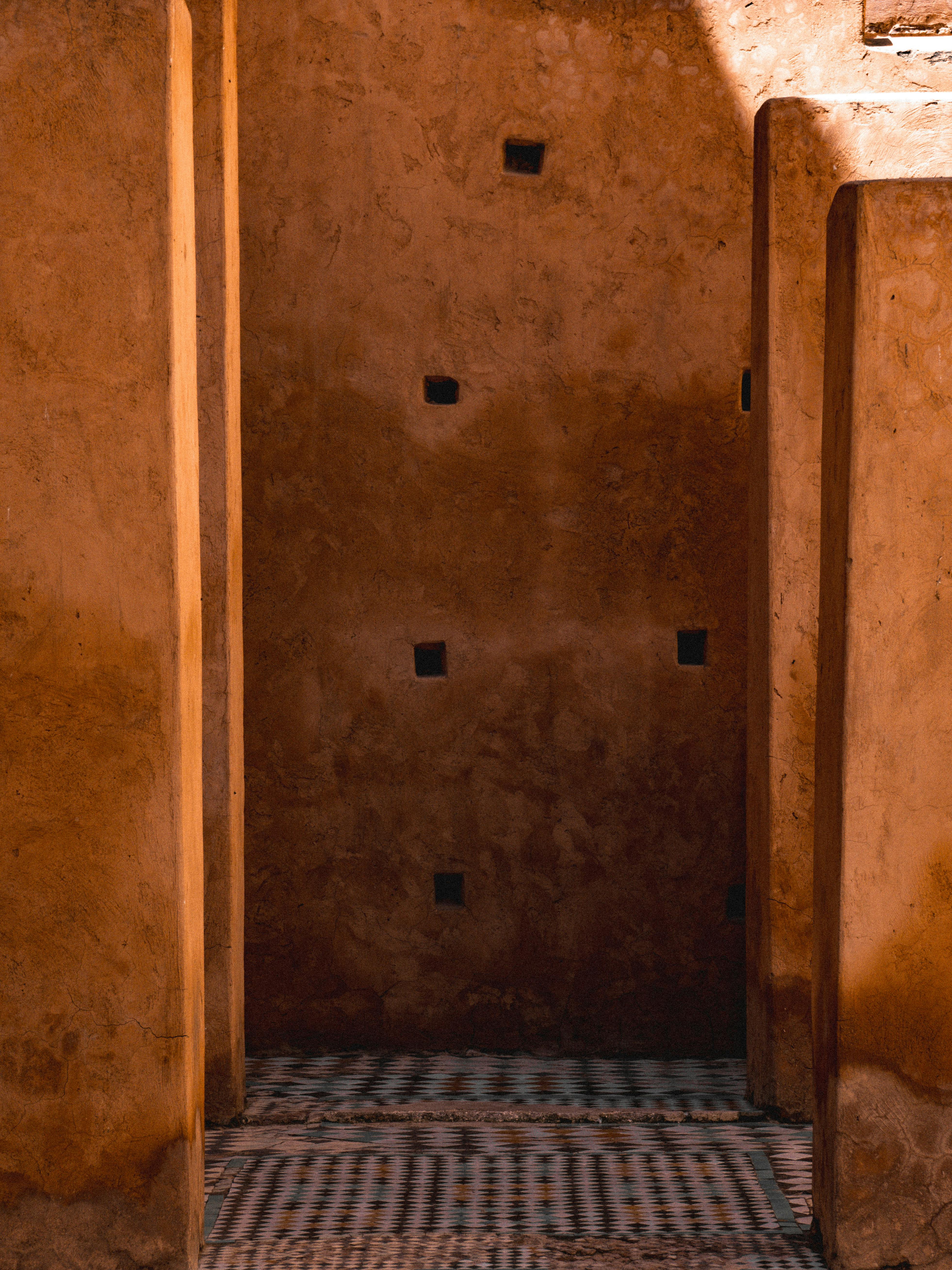 бесплатная Теплый солнечный свет отбрасывает тени в узком марокканском проходе, подчеркивая текстуру саманных стен. Стоковое фото