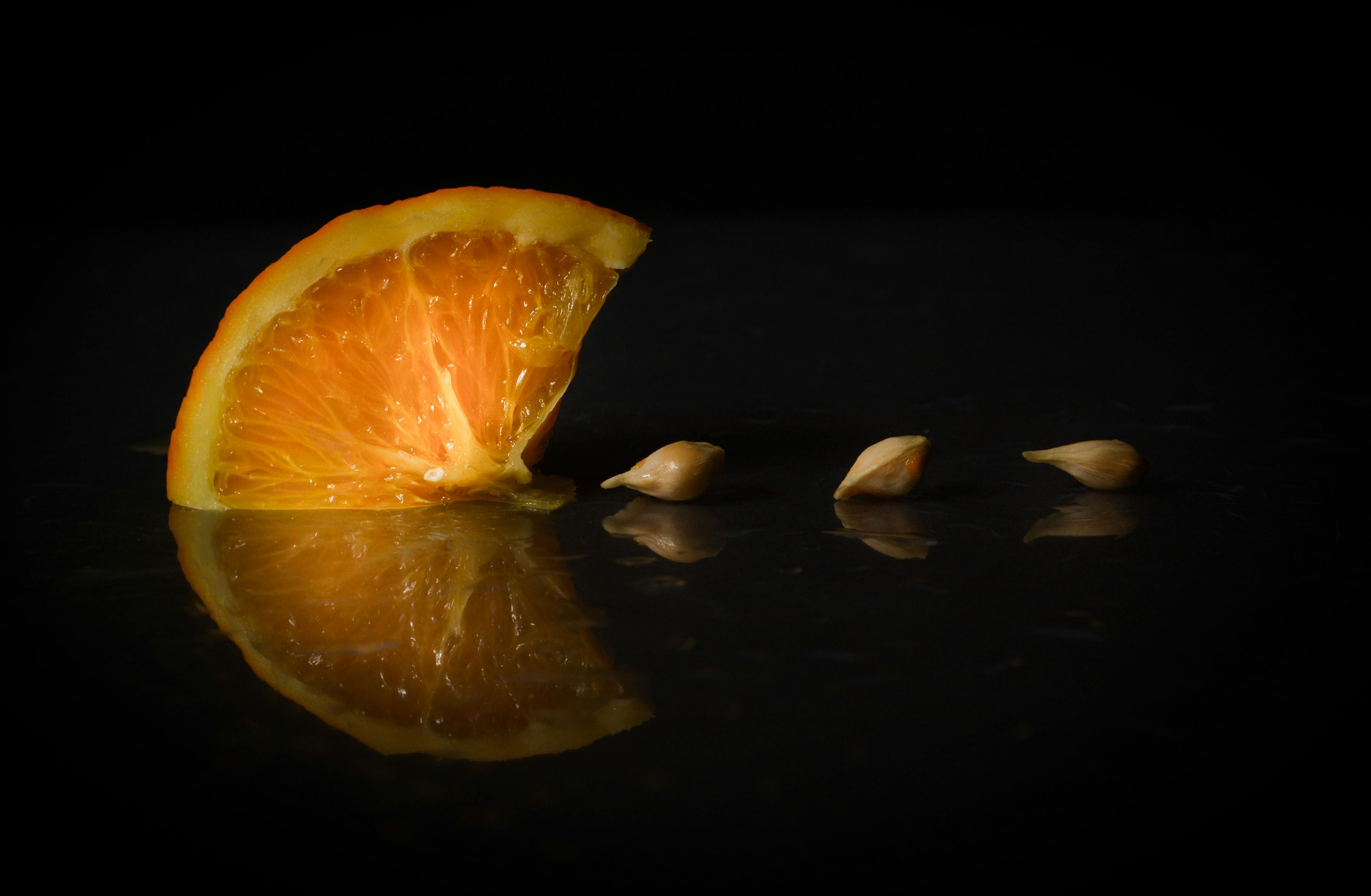 Free A fresh orange slice with seeds on a reflective surface in low light. Stock Photo