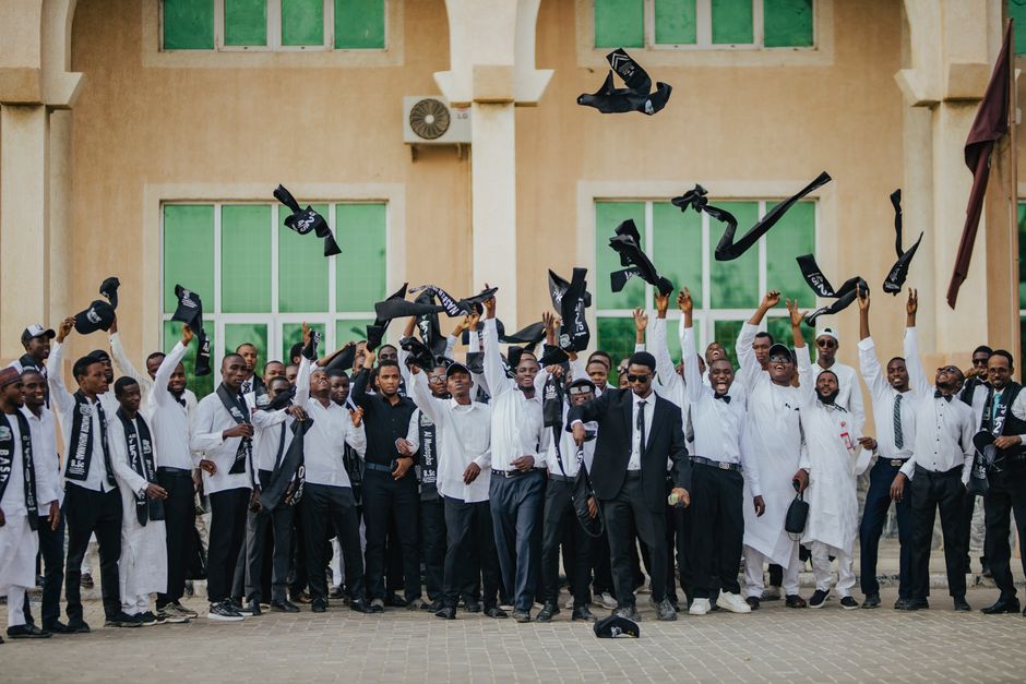 A joyful group of graduates in formal attire celebrating by tossing caps outside a building. A joyful group of graduates in formal attire celebrating by tossing caps outside a building.