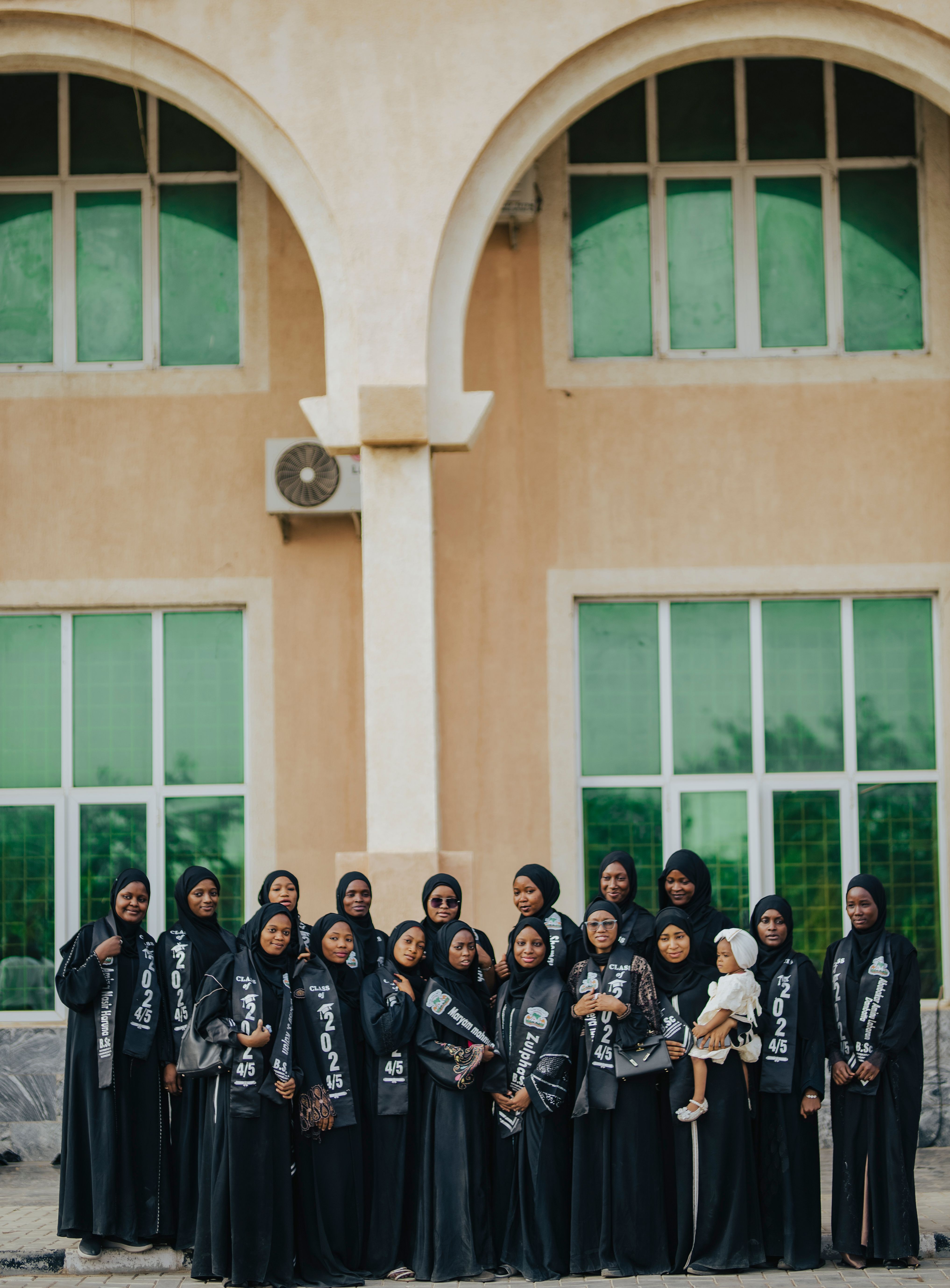 A large group of women in black traditional attire standing outside a classical building.