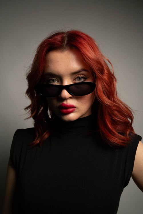 Free Modern portrait of a red-haired woman wearing black sunglasses and a sleeveless top. Stock Photo