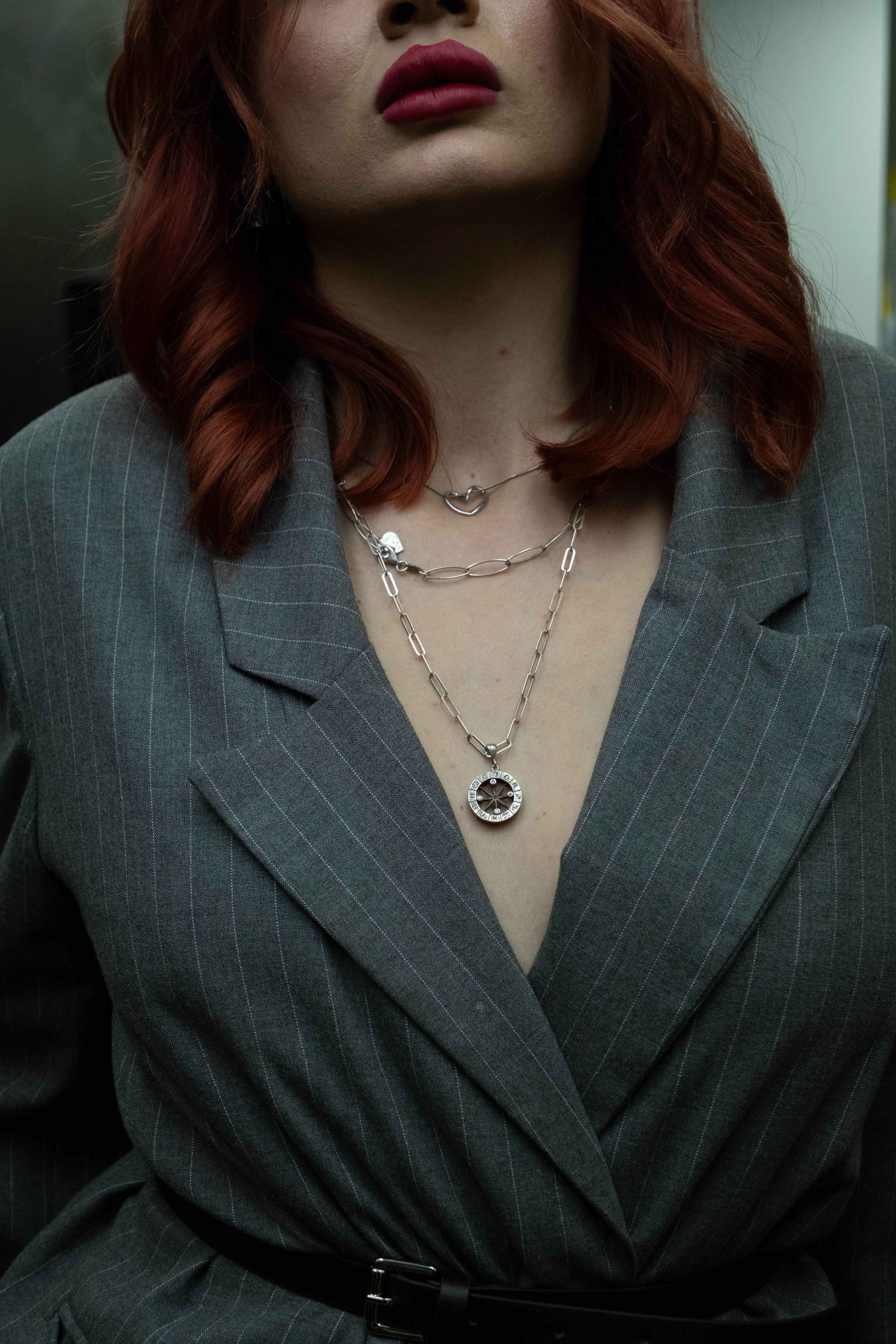 Retrato estiloso com uma modelo usando um blazer listrado e lábios vermelhos vibrantes, exibindo colares em camadas.