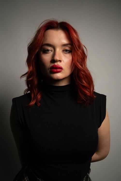 Free Portrait of a woman with red hair and bold lipstick in dim lighting. Stock Photo