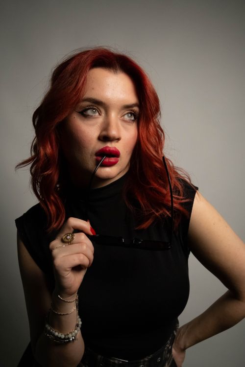 Free Stylish woman with red hair, deep red lipstick, posing indoors with sunglasses in hand. Stock Photo