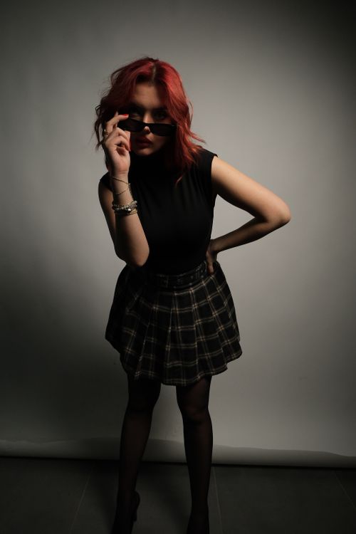 Free Stylish redhead woman posing with sunglasses, showcasing modern fashion in a studio. Stock Photo