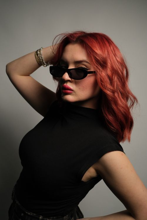 Free Woman posing with bold red hair and stylish sunglasses in a studio shot. Stock Photo