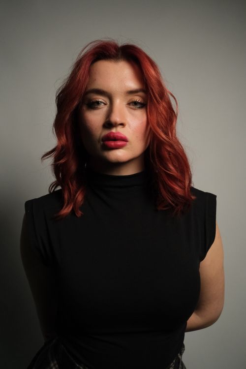 Free Stylish portrait of a woman with red hair in a black top, shot indoors. Stock Photo
