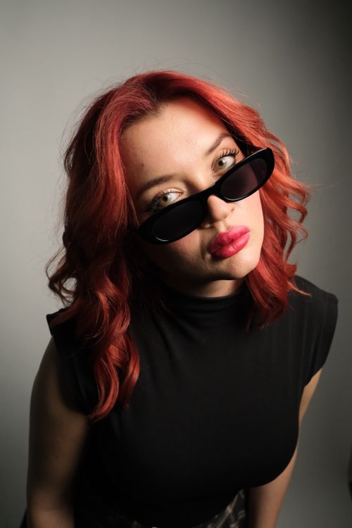 Free Stylish portrait of a woman with red hair, wearing sunglasses and a black outfit, fashion forward. Stock Photo