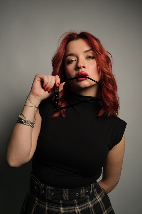 Free Portrait of a fashionable young woman with red hair and black outfit against a gray studio background. Stock Photo