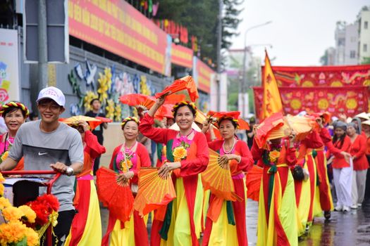 Vibrant outdoor parade featuring people in traditional Vietnamese attire with fans and flowers.