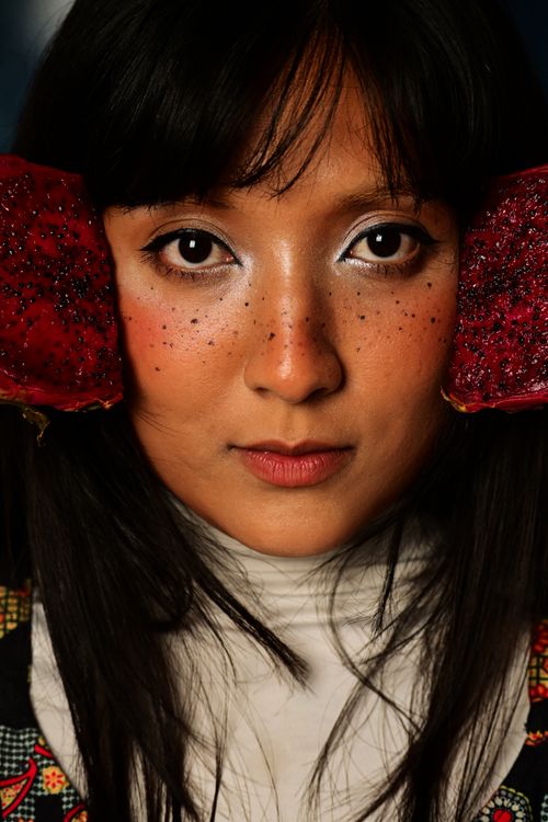 Free Close-up portrait of a woman holding dragon fruit slices beside her face, creative makeup. Stock Photo