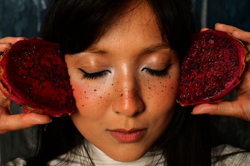 Free Close-up of a woman with eyes closed holding dragon fruit halves against her cheeks. Stock Photo