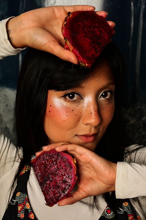 Free Artistic portrait of a woman holding vibrant dragon fruits with creative makeup. Stock Photo