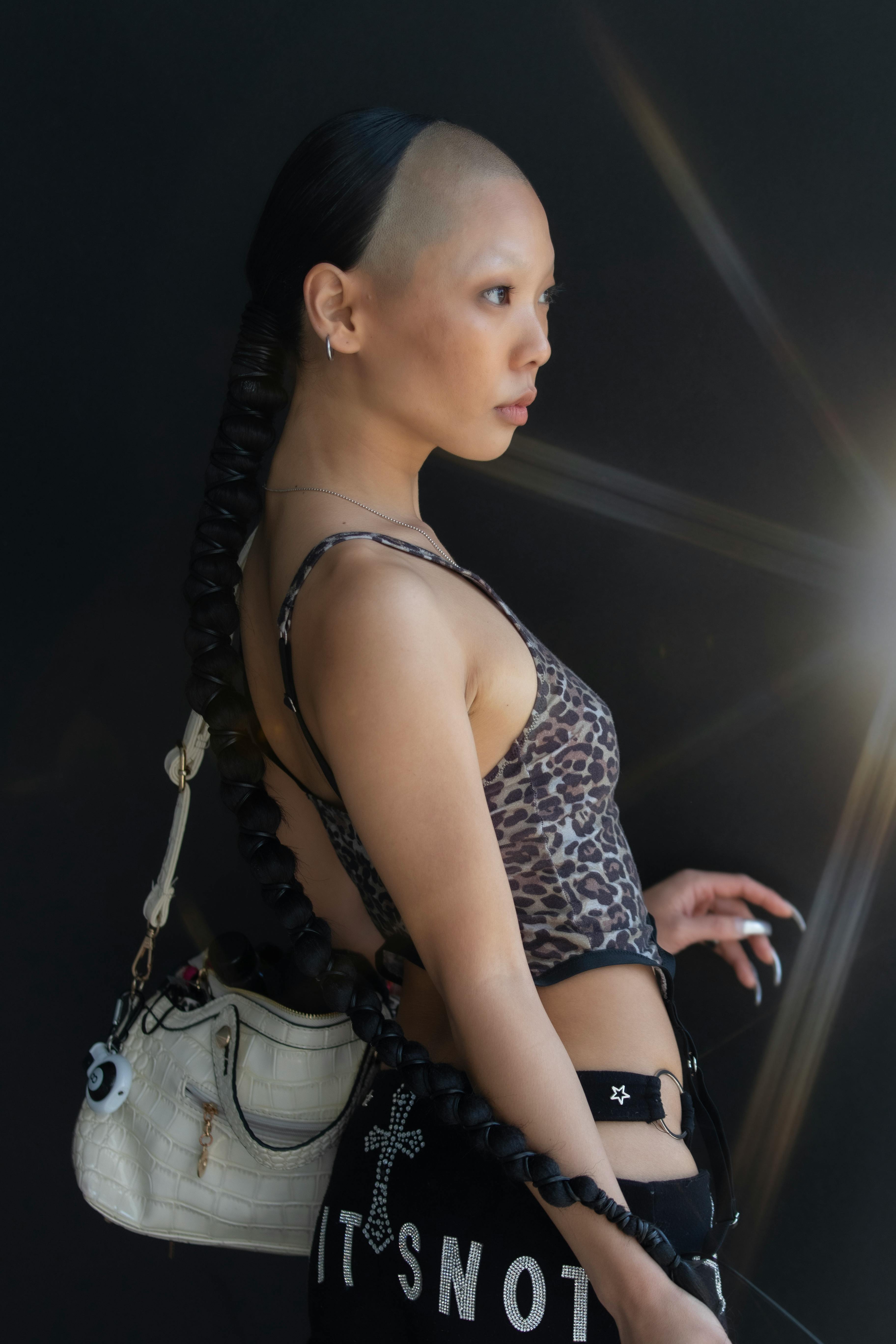 無料 暗い背景に、編み込みの髪、ヒョウ柄のトップス、エッジの効いたアクセサリーを身に着けたファッショナブルな女性。 写真素材