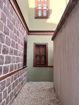 A narrow alleyway between traditional Turkish buildings featuring stone and stucco walls with wooden windows.