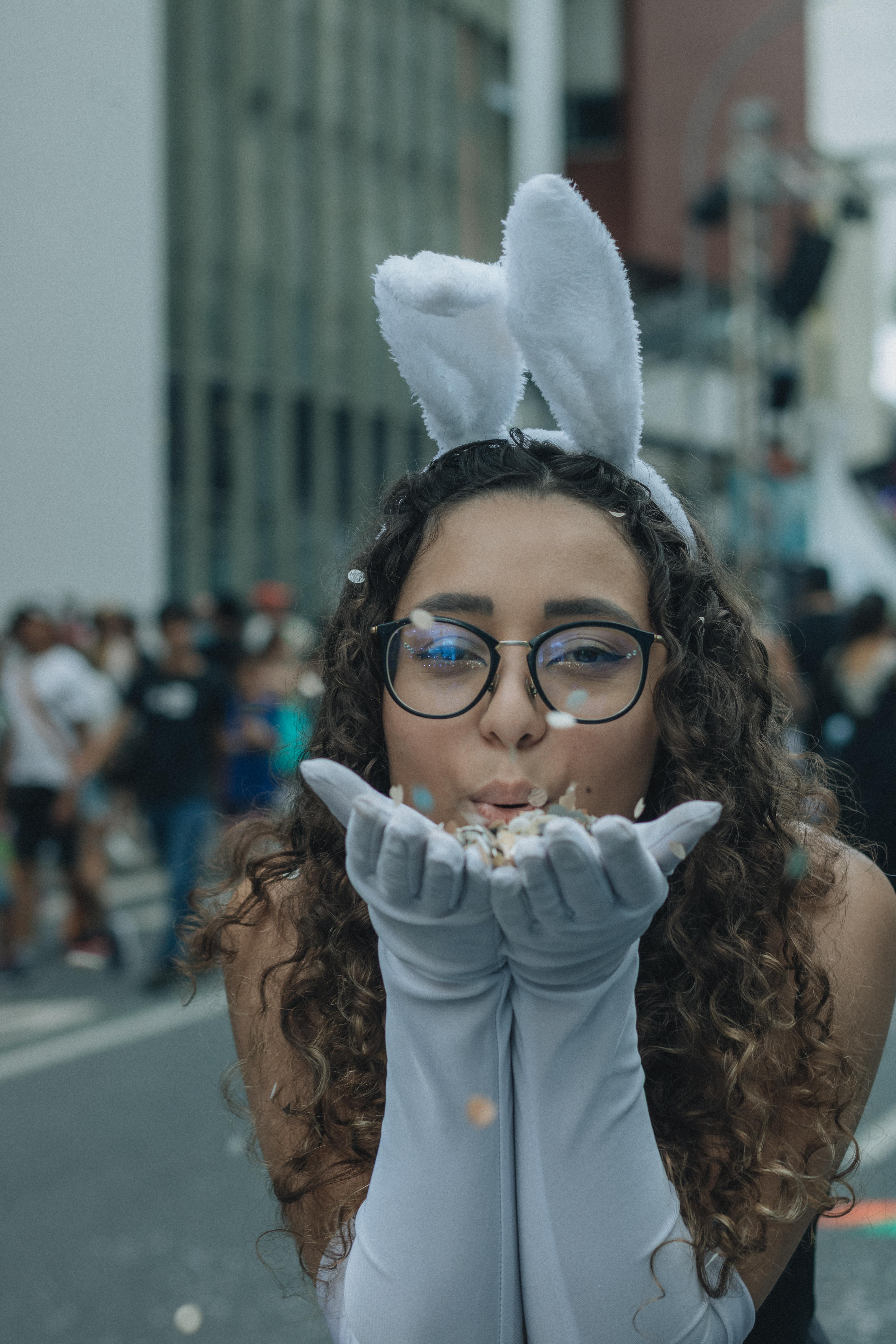 Kostenlos Eine Frau mit Hasenohren pustet bei einer Veranstaltung im Freien Konfetti und sorgt so für eine ausgelassene Atmosphäre. Stock-Foto