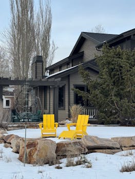 Winter scene of a rustic house with yellow chairs in a snowy garden in Park City, Utah.